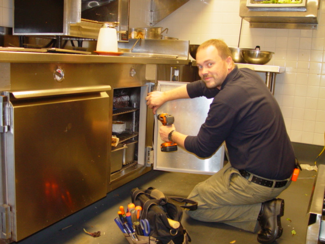 A Gasket Pro technician smiling while refitting an undercounter refrigerator door in a commercial kitchen.